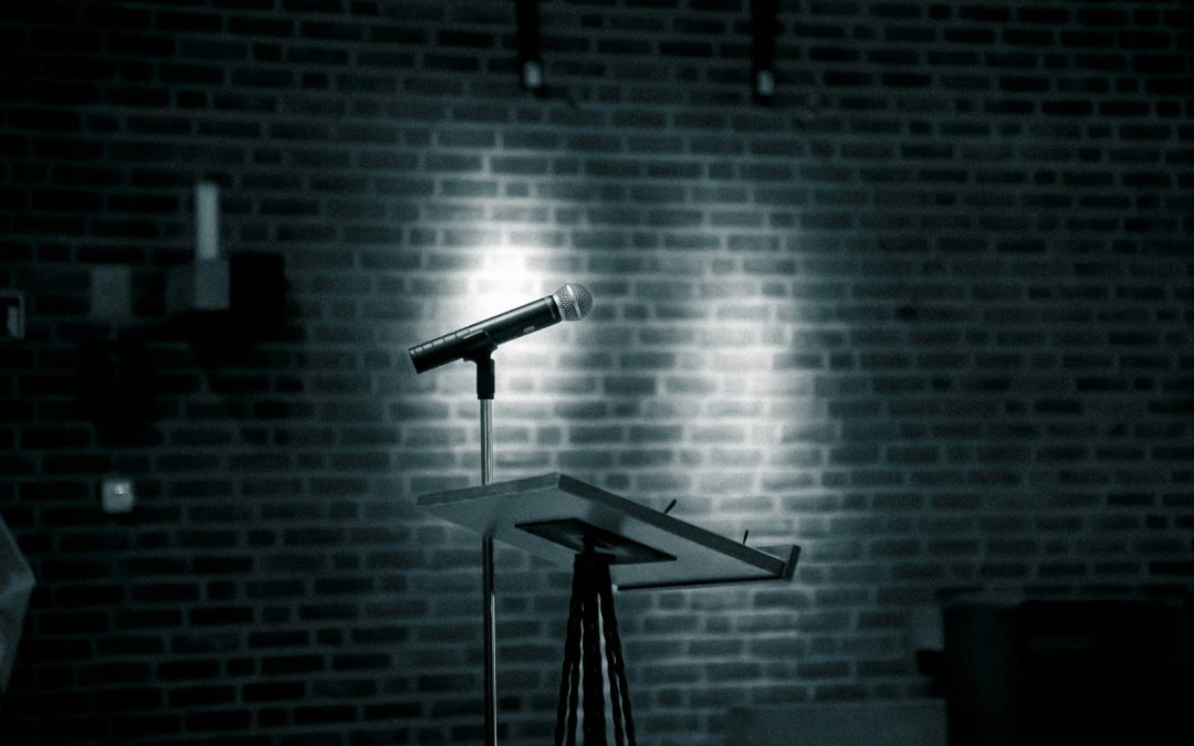 Empty microphone under a spotlight on a brick comedy club stage, representing every open mic night mapped and searchable on OnlineOpenMic.com in 2026